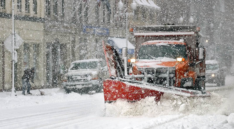 CLEANING UP: A snow shoveler, left, and a City of Augusta plow truck both do their parts to clear snow on Water Street this afternoon in downtown Augusta.