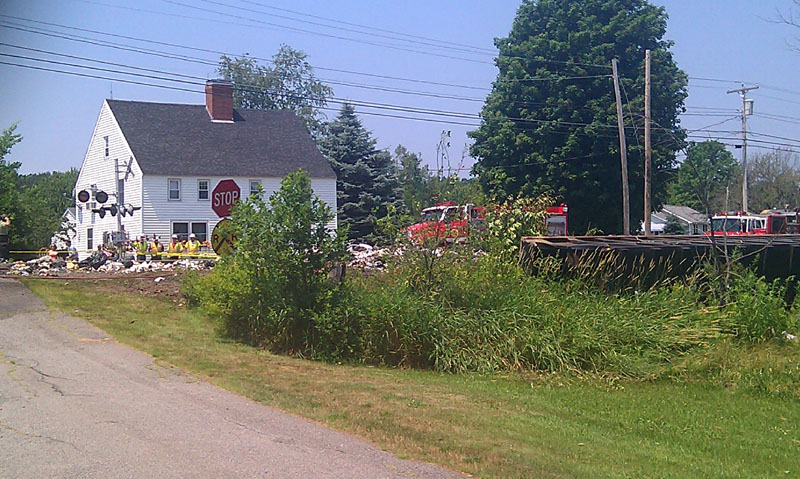 A view of the collision scene showing part of the railroad crossing at Route 4 and Buffum Road at left, and the trailer of the truck that was hit lying on its side in the grass at right.