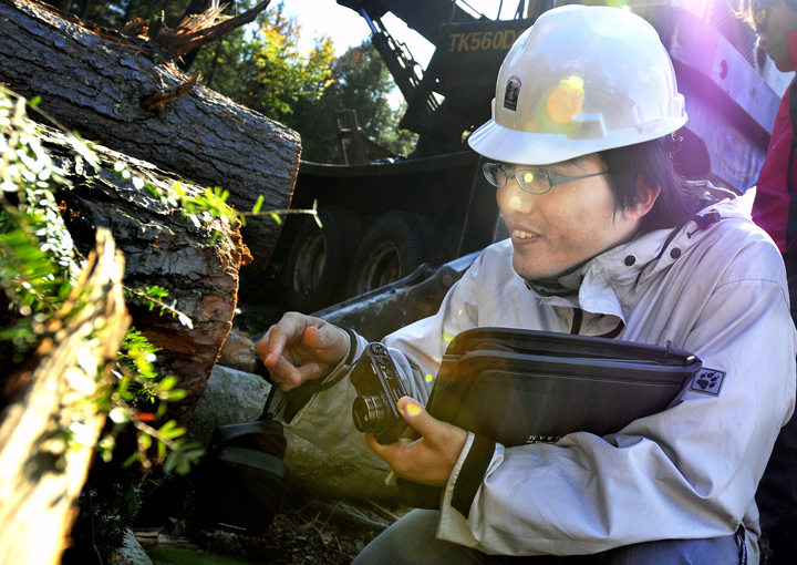 Ohchi Shunsuke of Japan examines a log Monday at a 50-acre property in Brunswick being harvested by Maine Custom Woodlands, a certified master logging company in Durham.