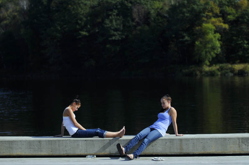 AUTUMN SUN: Kassie Bryant, left, and Heidi Moore soak up the rays Sunday at the bulkhead on the Kennebec River in Hallowell. The Augusta 20-year-olds were sunning in fall temperatures in the 80s. “It’s amazing,” Bryant said of the mild weather.