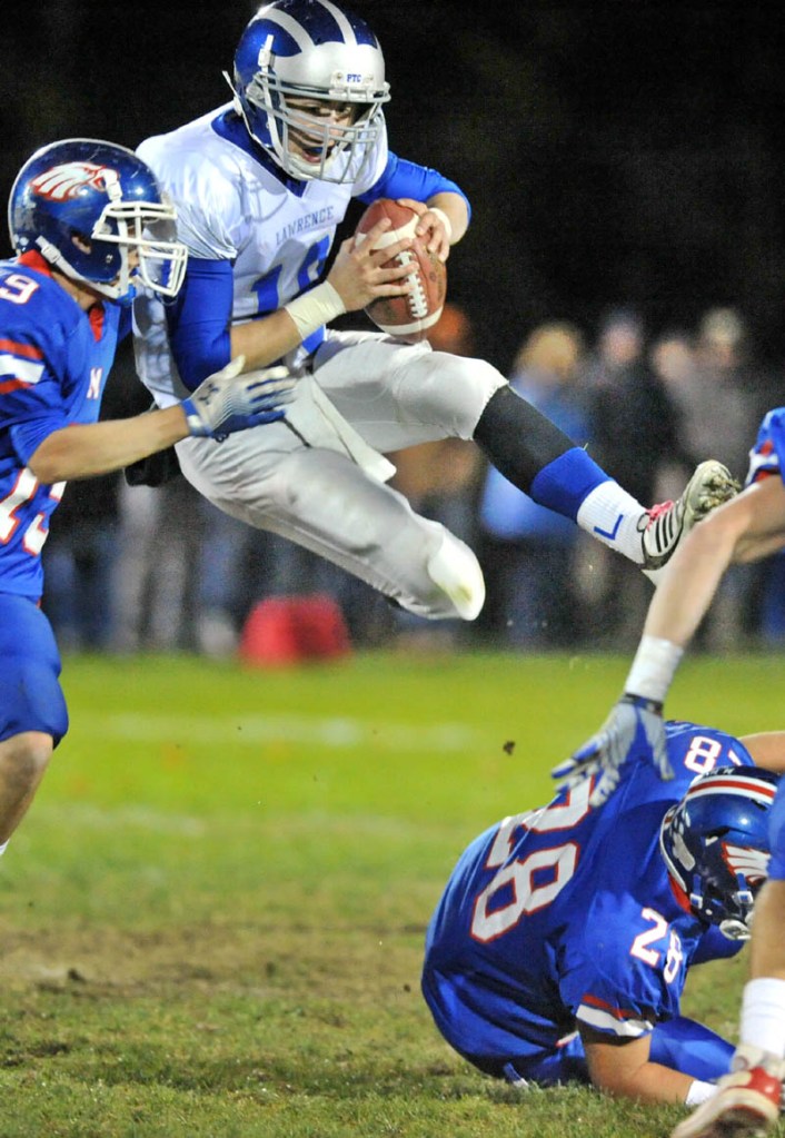 Lawrence High School quarterback Alex Leathers, 19, leaps over Messalonskee High school defender Corey Foye, 28, as Travis St. Pierre, 19, left, pursues in the second quarter at Messalonskee High School in Oakland Friday night.