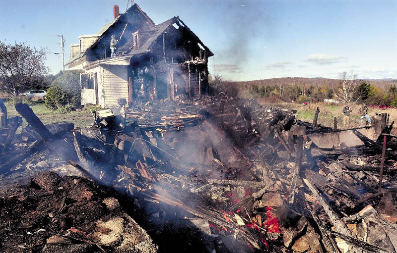 Athens firefighter Jeremy Farmer searches for hot spots on the second floor of the home of Doug and Mary Lou Harlow that caught fire Tuesday evening. Portions of the home and a barn, still burning in foreground, were destroyed.