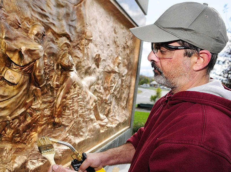 FINISHING UP: Anthony Tafuri, of Pro Point Restoration, paints on chemicals and uses a torch to add a patina to the recently cleaned plaques on the Civil War monuments Tuesday in Augusta’s Memorial Circle. Pro Point, a company from Pittsfield, N.H., has been working for about a month on repointing the stones and cleaning and adding a patina to the plaques.