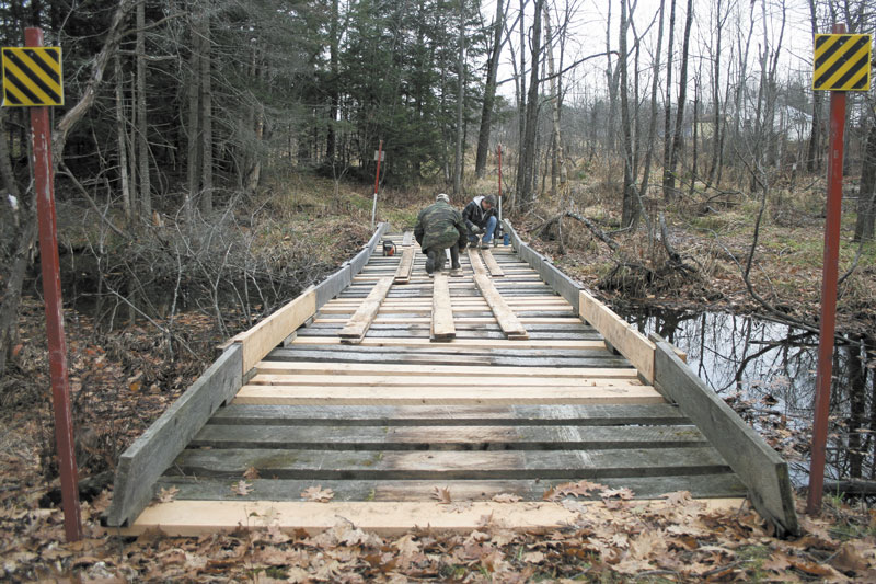 PUTTING IN WORK: Robert Bickford and Eric Roberts, members of the Central Maine Snowmobile Club, repair a snowmobile bridge Sunday in Waterville. Due to a shortage of volunteers, the two men perform all of the yearly maintenance on Waterville's trail system. Many of Maine’s 287 snowmobile clubs have difficulty finding volunteers to maintain the state's 14,000-mile trail system.