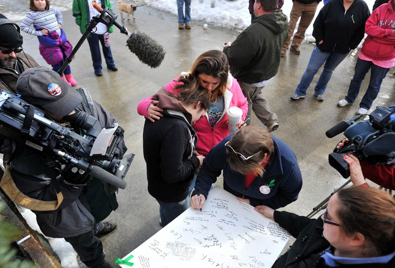 Staff photo by Michael G. Seamans Trista Reynolds, center left, is comforted by a friend, Amanda Benner, center, as Reynolds mother Becca Hanson, center right, signs a message on a board of well-wishes during a vigil in Castonguay Square in Waterville for missing toddler, Ayla Reynolds Saturday.