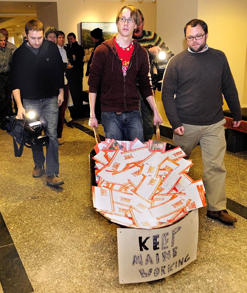 Staff photo by Joe Phelan Matt Caston, center, and Charlie Urquhart, of Working America, are followed by videographers as they deliver a wheelbarrow of post cards to Gov. Paul LePage's office in the Augusta's State House on Wednesday morning.