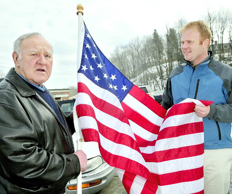 Jim Keenan, left, and Patrick Wright, executive director of Gardiner Main Street, hold up an American flag Keenan bought to show as example for his project of lining U.S. Route 201 in the city with them.