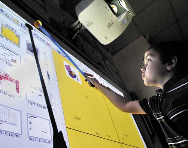 ADVANCES IN LEARNING: First-grader Conner Easter uses a wand to click a part of screen he can’t reach on the SmartBoard during a recent demonstration for parents and donors in Maureen Cooper’s class at Gilbert School in Augusta. The projector for the board can be seen above him.