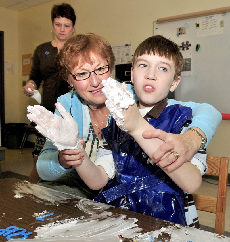 Winslow Elementary student Will Weiss reacts during a sensory exercise using shaving cream and rubber toys as education technician Linda Lemieux works with him. Special Education teacher Amy Benham observes others in the class for students with autism.