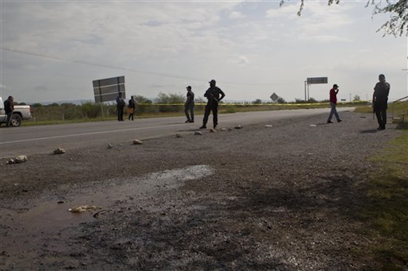 Federal police guard as forensic experts examine the area where dozens of bodies, some of them mutilated, were found on a highway connecting the northern Mexican metropolis of Monterrey to the U.S. border in the town of San Juan near the city of Monterrey, Mexico, Sunday, May 13, 2012. (AP Photo/Christian Palma)