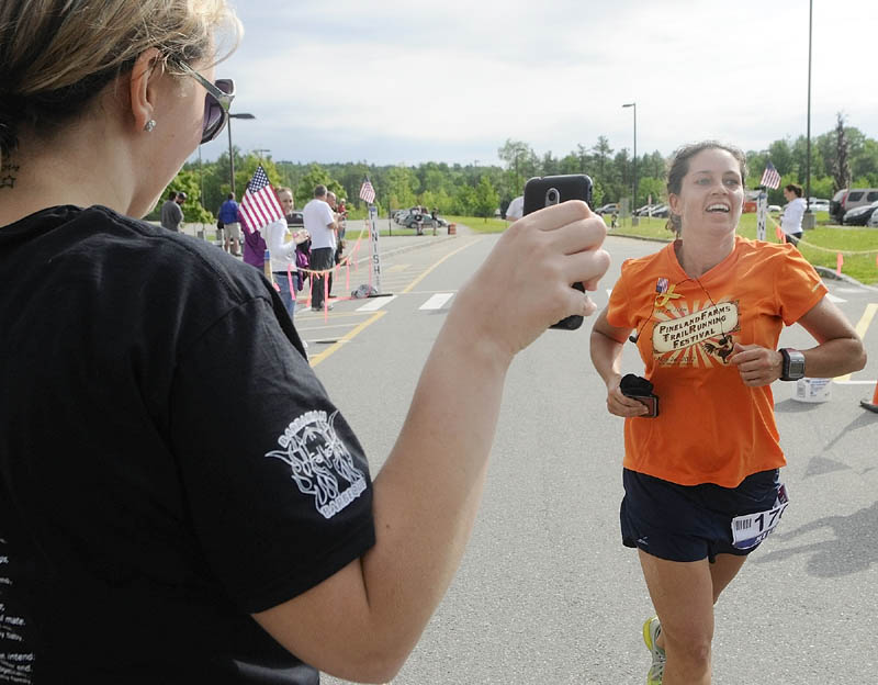 First female finisher Rebecca Miller, right, crosses the finish line as Meghan Niles, left, holds up her smartphone so that Staff Sgt. Travis Mills can watch the Miles for Mills 5K on his laptop in his hospital room in Bethesda, MD.