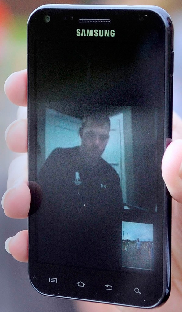 Staff Sgt. Travis Mills watches the Miles for Mills 5K from a hospital from a laptop in his hospital room in Bethesda, MD, as Meghan Niles holds up her smartphone.