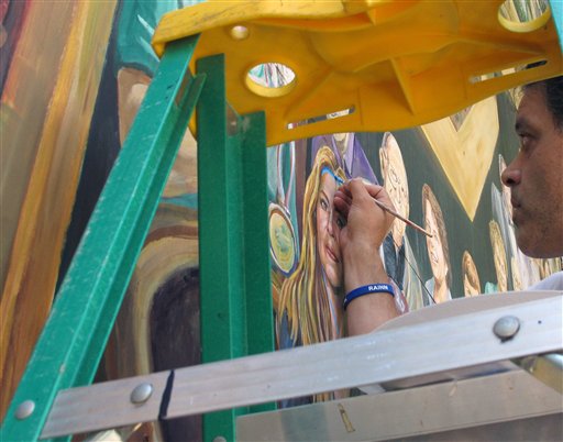 Artist Michael Pilato paints a blue ribbon on his mural in State College, Pa., on Monday.