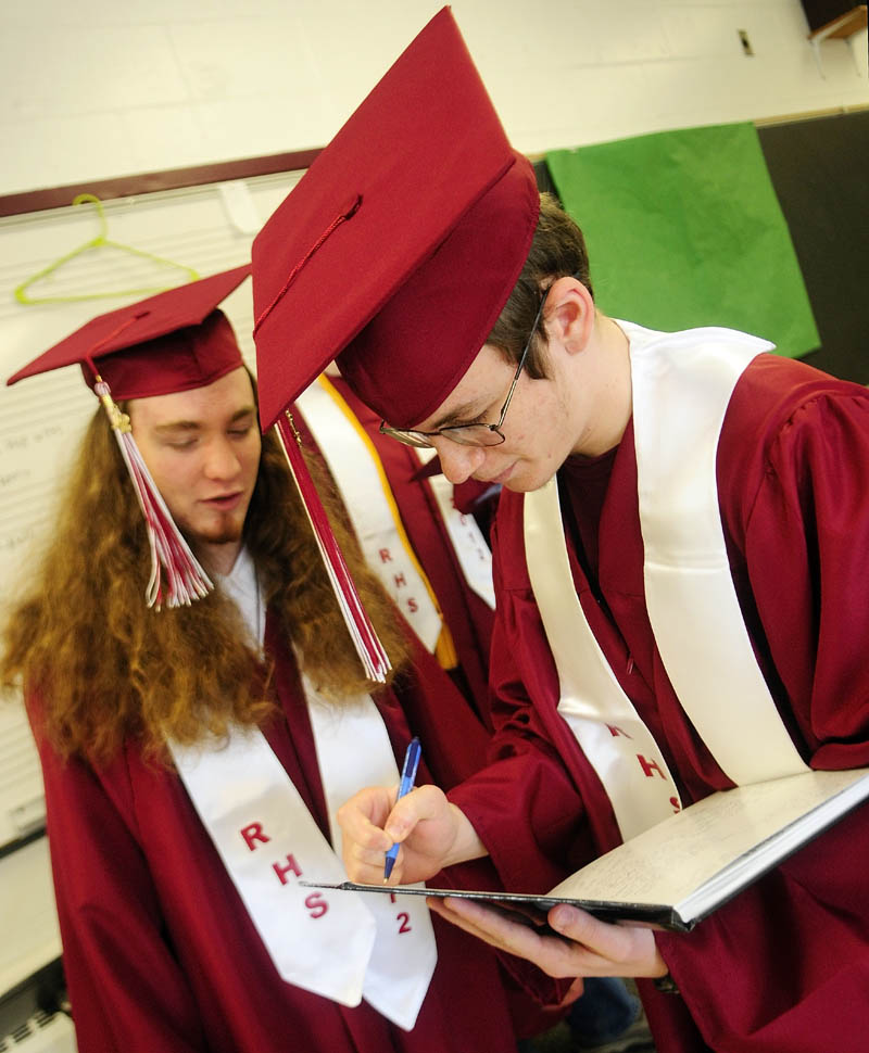 Sloan Hanning, left, watches as Jared Bowie signs his yearbook for him on Saturday afternoon before graduation at Richmond High School. There were 28 students graduating at the ceremony.