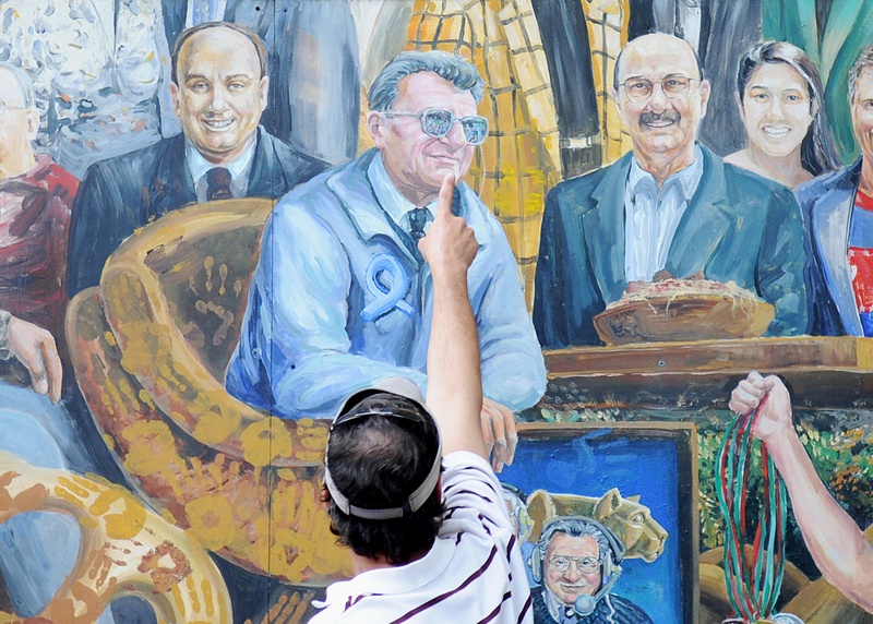 A visitor points to the spot in a mural where a halo that was above the late Penn State football coach Joe Paterno has been painted over by the artist in State College, Pa. on Saturday.