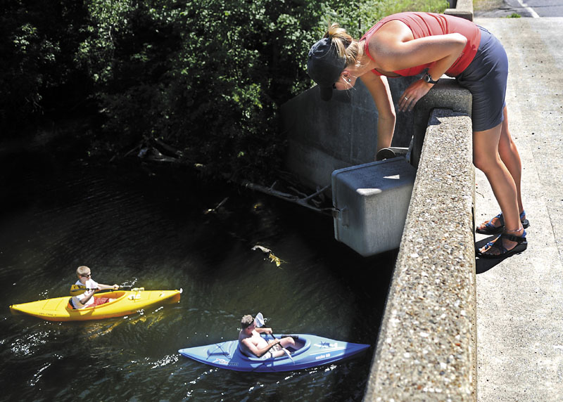 Cobbossee Watershed District intern Hannah Shute checks the gauge Thursday that measures the level of Annabessacook Lake in Monmouth as kayakers paddle beneath the bridge spanning it. The district is responsible for managing water levels and quality in the 28 ponds and lakes of the watershed. Shute, a student at the University of Southern Maine, is working for the district for the summer.