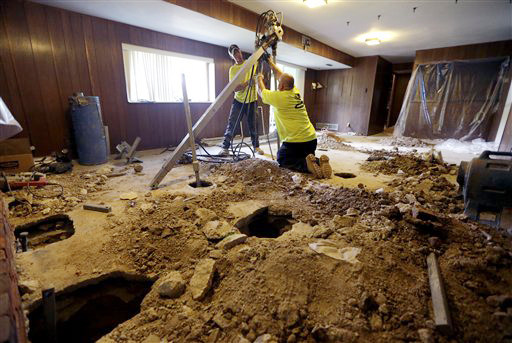 Corey Grotefendt, left, and colleague Don Baykowski drive piers into the ground in an effort to stabilize the foundation of Carl DeVaughan's settling home on Wednesday in Manchester, Mo.