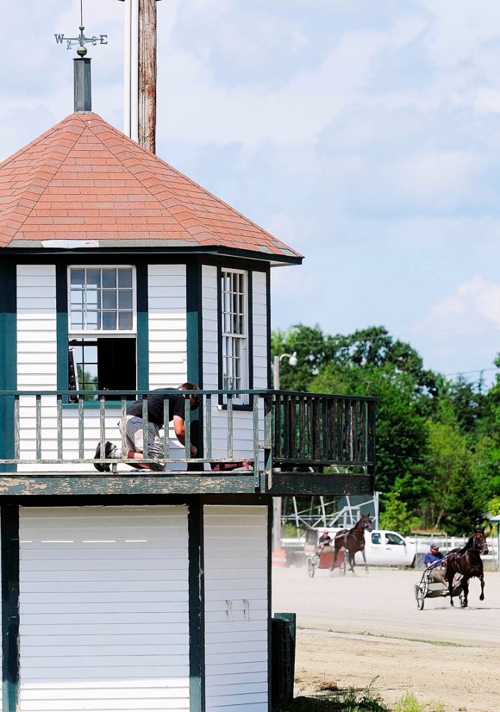 Drivers exercise their horses as Ryan Brann paints the small hexagonal building inside the track at Windsor Fairgrounds on Tuesday in Windsor. Brann and other workers are getting the fairgrounds ready for this year's annual Windsor Fair, which starts Sunday, Aug. 26.