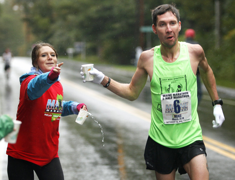 Mike Morris of Terre Haute, Ind., receives a cup of water from Sarah Kurland, a race volunteer from the Greely High cross country team, at a water station on Route 88 in Cumberland.