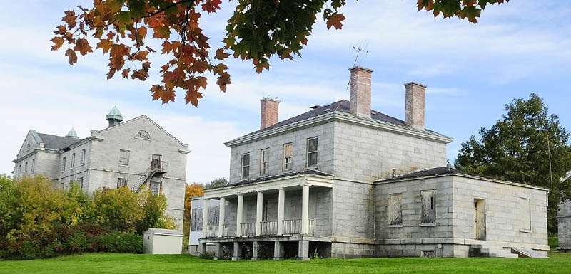 The doors and windows of the the riverfront granite buildings of the Kennebec Arsenal have been boarded up for years.