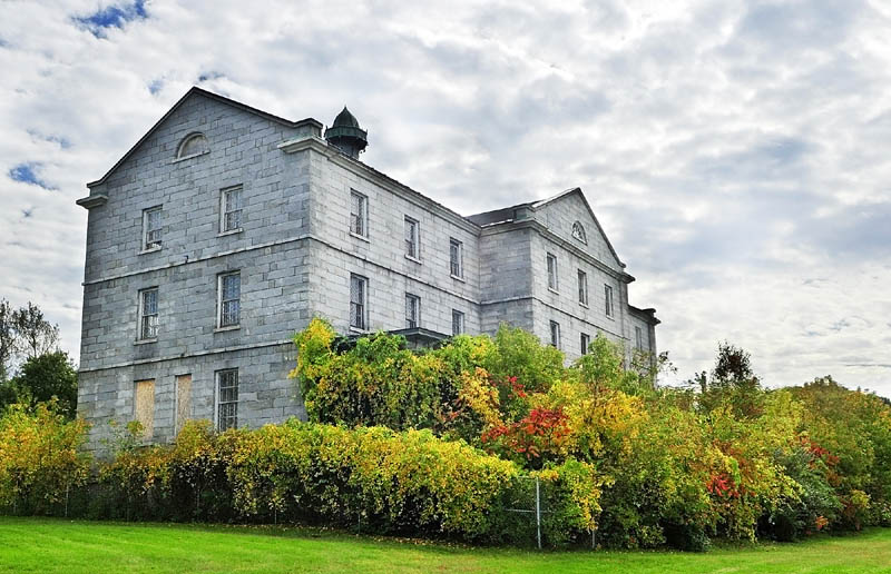 The doors and windows of the the riverfront granite buildings of the Kennebec Arsenal have been boarded up for years.