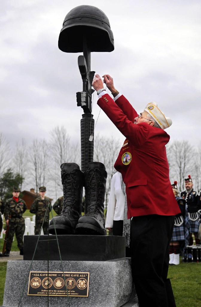 Disabled veteran Richard Fournier hangs dog tags Sunday on the new Battlefield Cross Memorial Monumentn during a dedication ceremony at the Maine Veterans' Memorial Cemetery in Augusta.