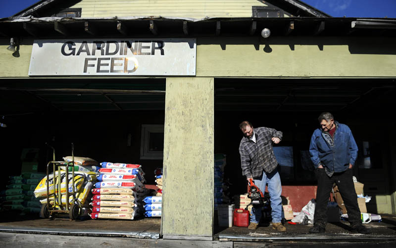 George Brown, left, starts a chainsaw Monday, with Wayne Cross on the loading dock of Gardiner Feed. Cross sells saws, which Brown services, at the livestock supply store he's operated for 40 years, at the confluence of Cobbossee Stream and the Kennebec River.