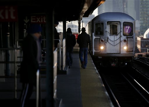 Commuters walk on the platform as a train enters the 40th Street-Lowry Street Station, where a man was killed after being pushed onto the subway tracks, in the Queens section of New York on Friday.
