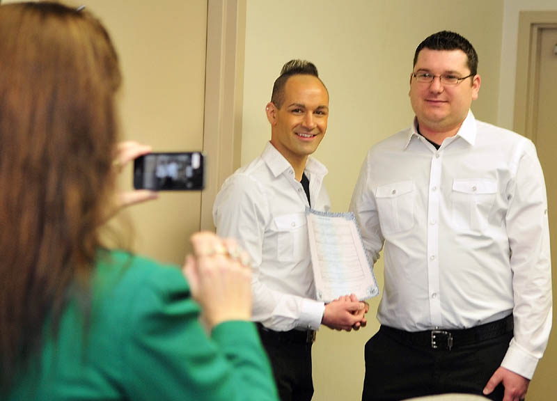 Maria Berube, left, snaps a photo of Lance Wallace, left, and her stepson, Sebastien Wallace, holding up their marriage certificate following the couple's wedding this morning in the Gardiner City Council chamber.