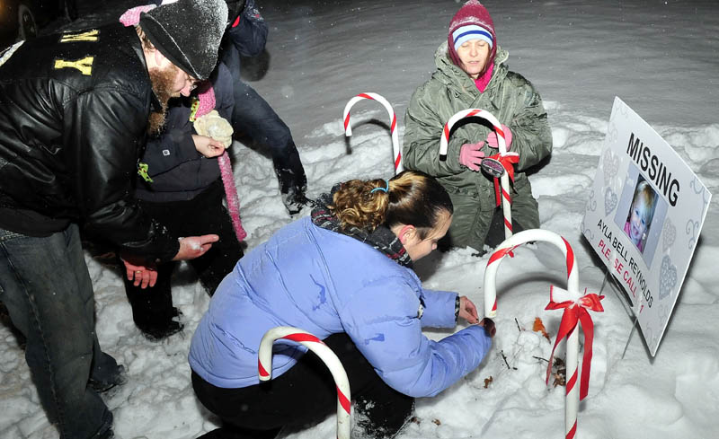 Vigil organizer Karen Francis and others place candles at the base of a lawn sign, bearing a photo of missing toddler Ayla Reynolds, outside 29 Violette Ave. in Waterville on Monday. Reynolds was reported missing from the home one year ago.