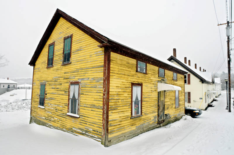 The exterior of 25 Bond Street in Augusta. The yellow house has been boarded up for many years, with trompe l'oeil paintings by Jane Burke depicting curtained windows and one has a man waving from inside.