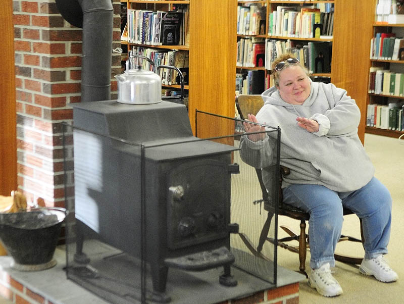 Denisa Laflamme, of Lewiston, warms up beside the wood stove at the Vassalboro Public Library Wednesday. The wood stove is part of the library's logo. Hours are Mondays and Wednesday from 12:30 to 8 p.m., and Saturday's from 10 a.m. to 6 p.m.