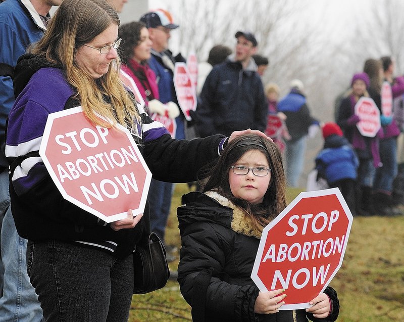 Christina Biegeleisen, left, and her daughter Makayla Biegeleisen, 8, both of South Paris, hold signs on the east side of the Capitol building during a Hands Around the Capitol event Saturday at the State House in Augusta.