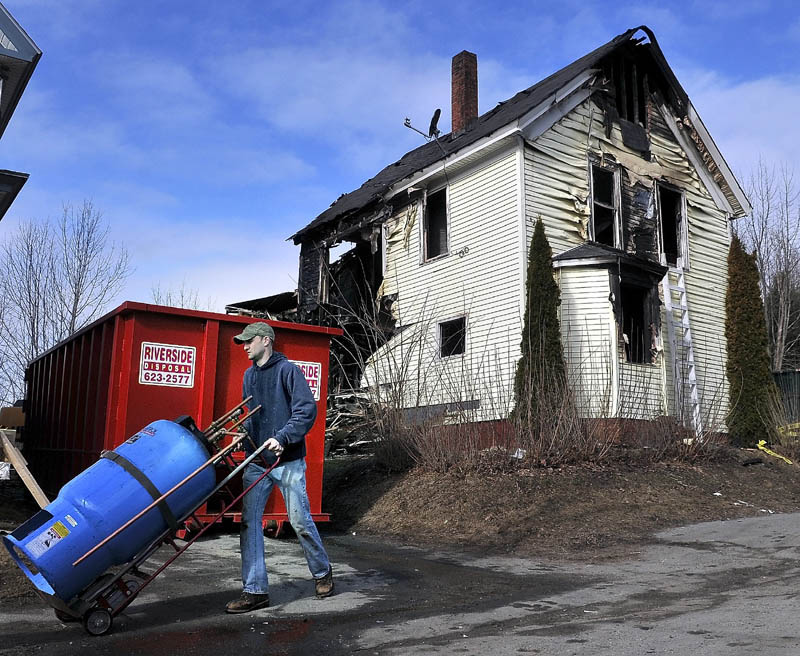 Rob Gay carts a boiler mate from the remains of 146 Northern Ave. in Augusta Monday, as crews raze the apartment building destroyed by fire on Thursday. Scott Laliberte, proprietor of Riverside Disposal, said the building would be down and removed by Tuesday, with the foundation filled in. Gay and other heating contractors removed the heating system from the building, to be installed in another building.