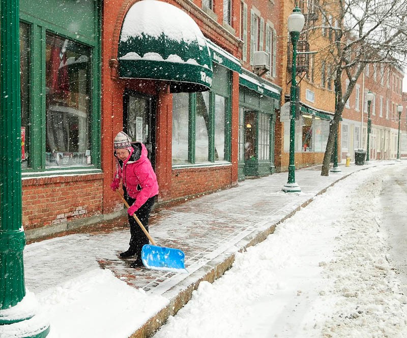 April Hall shovels snow from a late winter storm in front of the Reny's store, where she works, on Tuesday in Gardiner.
