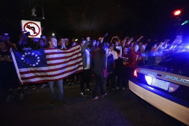 A police cruiser drives by as people react to news of the arrest of one of the Boston Marathon bombing suspects, Friday, April 19, 2013, in Boston. Boston Marathon bombing suspect Dzhokhar Tsarnaev was captured in Watertown, Mass. The 19-year-old college student wanted in the bombings was taken into custody Friday evening after a manhunt that left the city virtually paralyzed and his older brother and accomplice dead. (AP Photo/Julio Cortez)