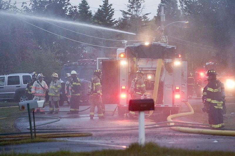 Firefighters wait outside the home of Charles Scontras after Saturday’s standoff with police. Scontras was presumed dead inside but authorities had yet to locate his body.