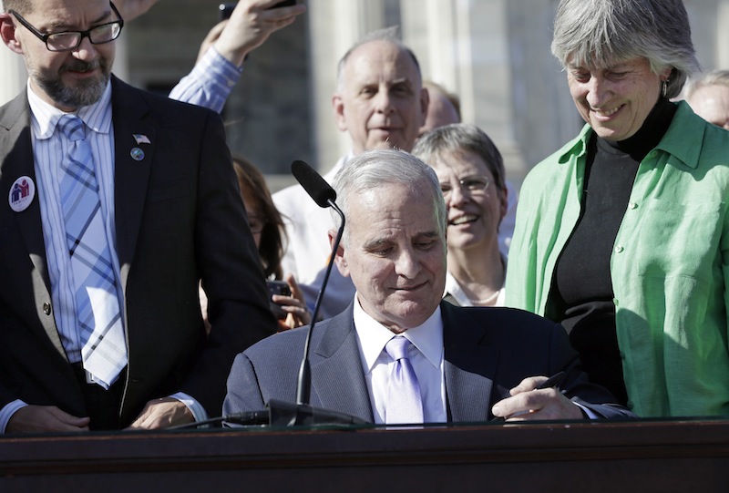 Minnesota Gov. Mark Dayton signs the gay marriage bill in front of the State Capitol Tuesday, May 14, 2013, in St. Paul, Minn. Minnesota becomes the 12th state to legalize gay marriage. Looking over Dayton's shoulder are bill sponsors, Sen. Scott Dibble and Rep. Karen Clark. (AP Photo/Jim Mone)