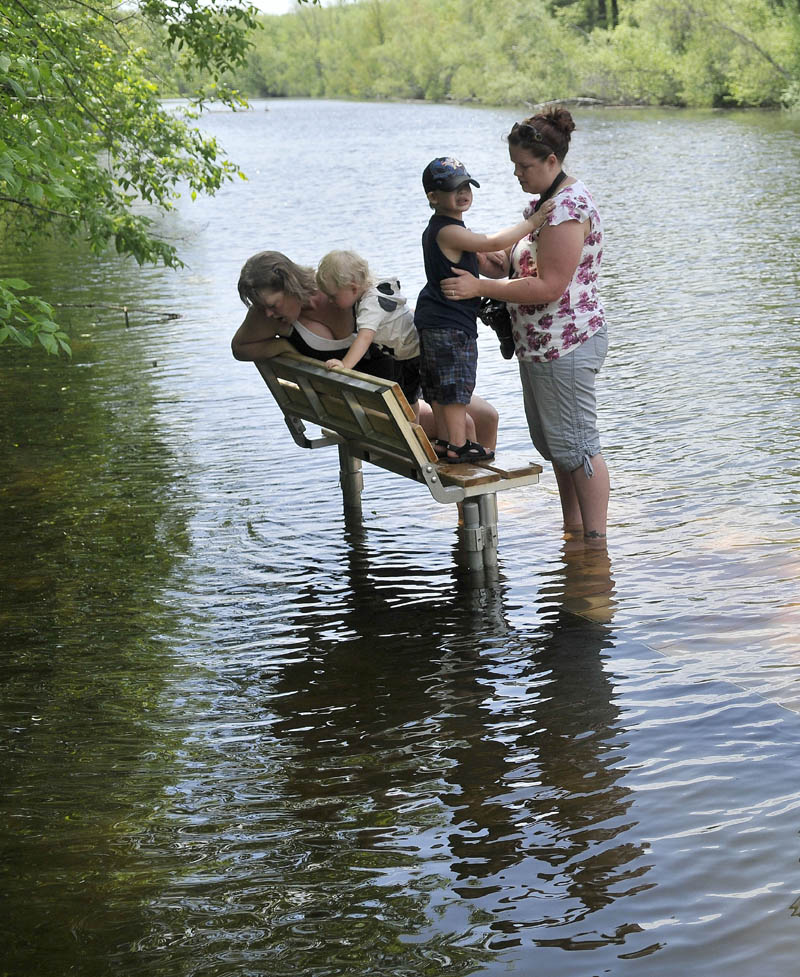 Laura St. Peter, right, stands with her son Vincent Tibbetts, 3, as Brandy Pouliot, far left peers into the swollen Messalonskee Stream from a bench on the new North Street boat launch dock on Thursday. After several days of rain the clouds broke ushering in more summer-like weather with the temperature touching 80 degrees for the next couple of days.