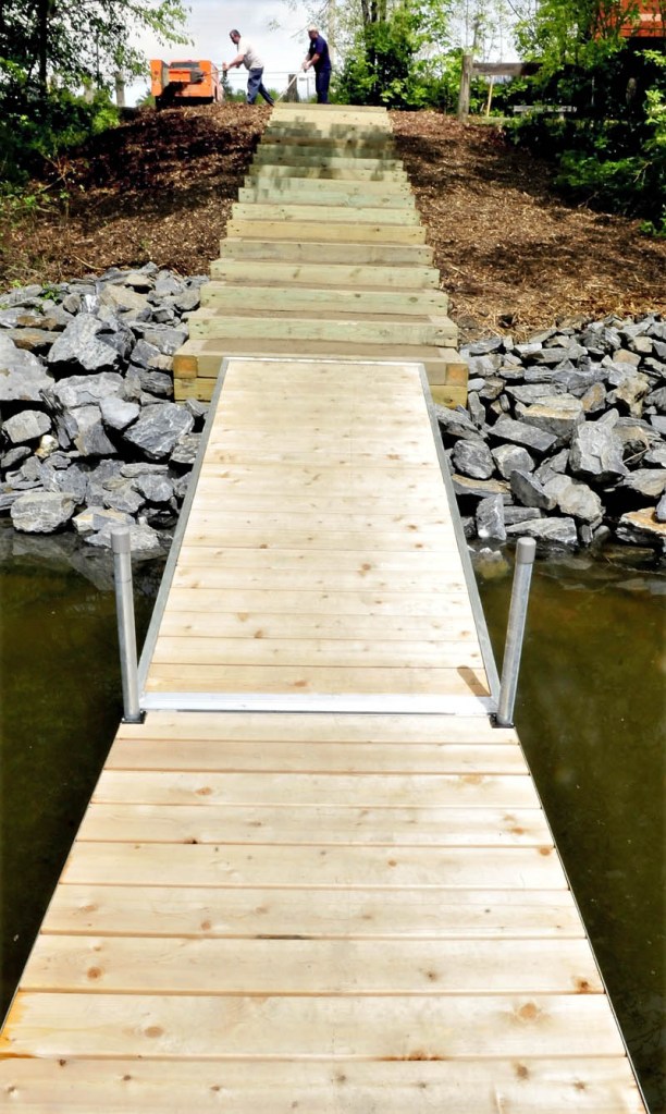 Mike Folsom, left, and Dan Wilson, of the Waterville Public Works department, rake bark mulch around steps to the new carry-in boat landing on Messalonskee Stream, off North Street, on Monday. The wooden structure replaces the slippery slope that boaters had to navigate before.