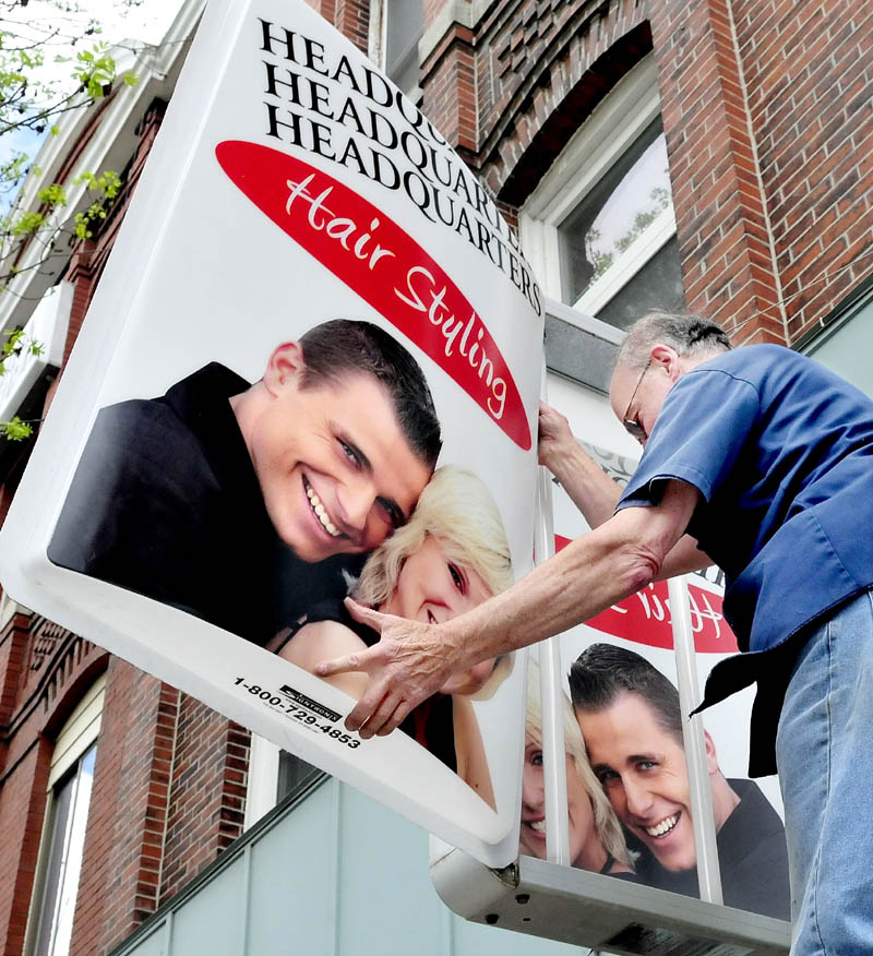 Mike Pellerin of Mike's Electrical Services installs one of two new signs at Headquarters Salon on Main Street in Waterville on May 13.