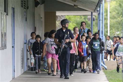 A Santa Monica police officer leads children on a field trip from Citizens of the World Charter School in Los Angeles out of Santa Monica College, where they had gone for a planetarium show, following a shooting in the area, in Santa Monica, Calif., Friday. Two people were found dead Friday in a burned home near the campus, where someone sprayed a street corner with gunfire.