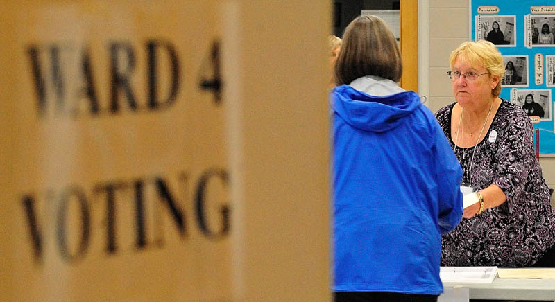 Co-warden Pat Seigny, right, hands a ballot to a voter on Tuesday June at the Ward 4 polling place in the Cony Middle School music room in Augusta.