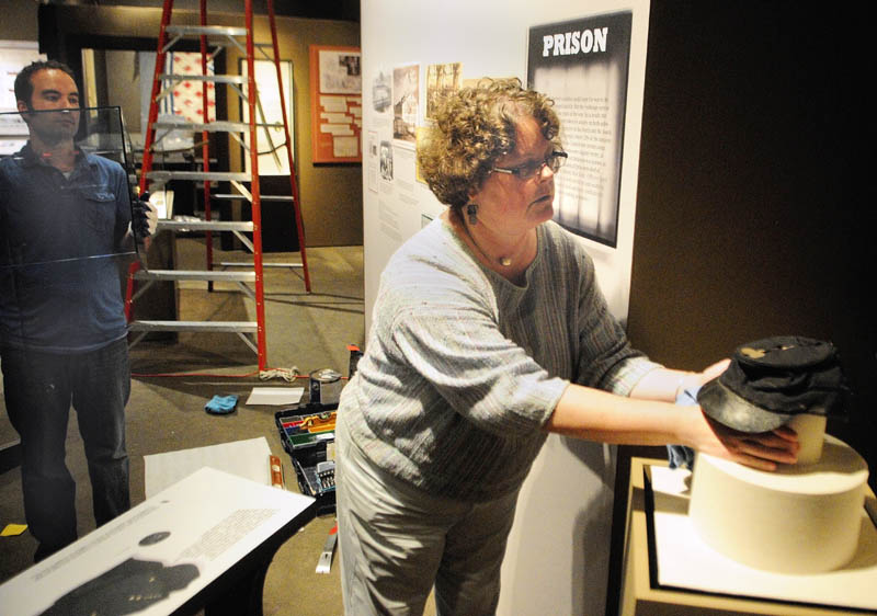 Facilities manager Aedan Jordan, left, waits with a vitrine to cover the forage cap that curator Laurie LaBar is positioning in the new exhibit, titled "Maine Voices from the Civil War," on at the Maine State Museum in Augusta.