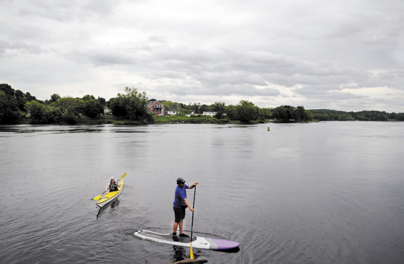 Eli Crispell, right, and Kate Browne explore the Kennebec River in Gardiner on a paddle board and kayak on Tuesday. The river furnishes several miles to explore by paddle.