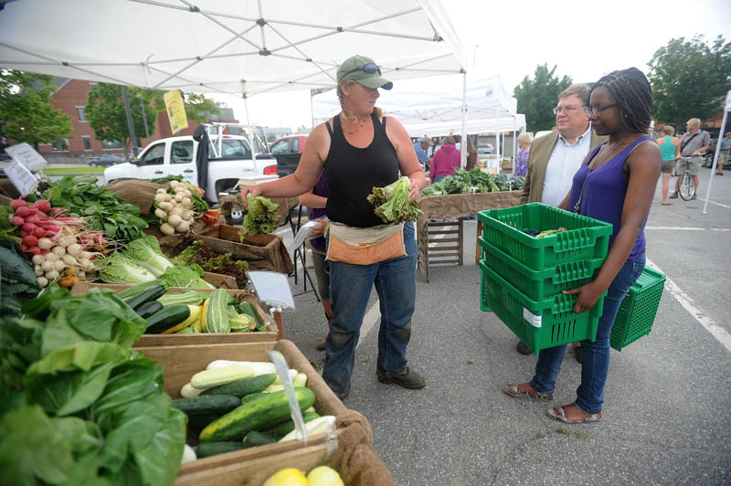 Hanne Teirney, left, with Corerstone and Fail Better Farms, offers organic produce to Noma Moyo, 21, a Colby College junior, right, and Joe Klaus, food services manager at Colby College, at the Waterville Farmers' Market at the Concourse on Thursday. Klaus, along with volunteer students, collect food from the farmer's market for distribution to local pantries.