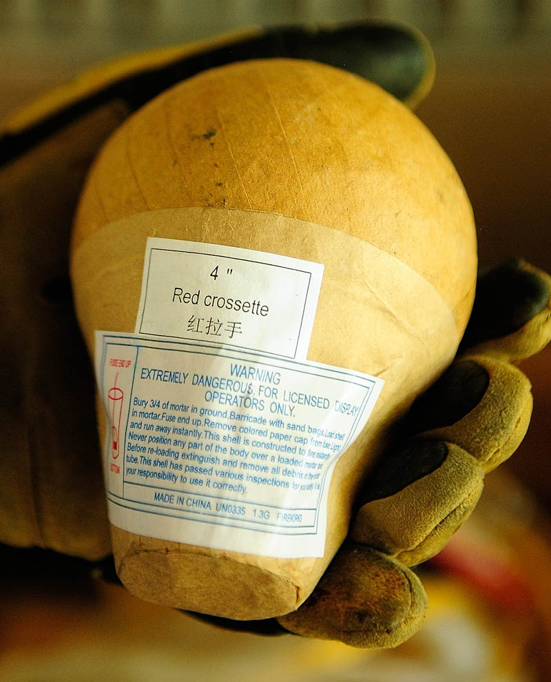 Charlie Squires holds up four-inch fireworks shell on Thursday at the Eastside Boat Landing in Augusta. The larger round top is the part that colorfully explodes in the sky and smaller base part is what launches it out of the tube.