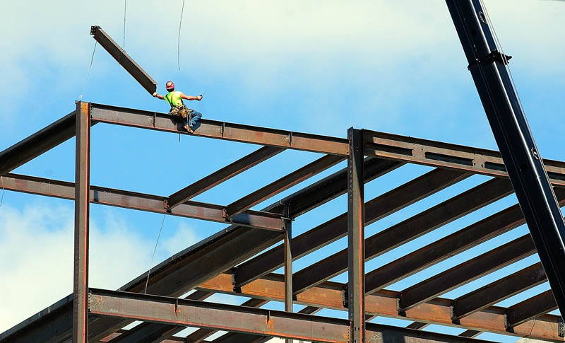A construction worker reaches for a beam being swung into place by a crane on Thursday at the site of the new Kennebec County Superior Court House being built in Augusta. The new building at the corner of Perham and Winthrop streets is behind the old court house.