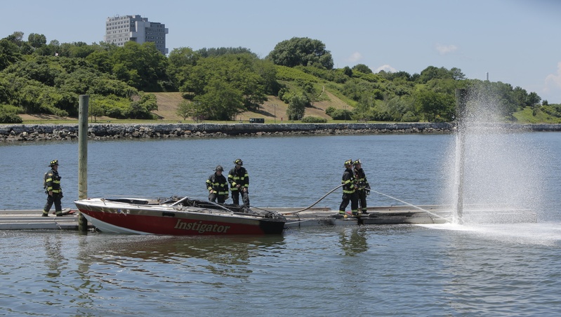 A Portland firefighter sprays foam on a piling at the East End boat dock in Portland where a boat, at left, exploded and caught on fire on Friday.