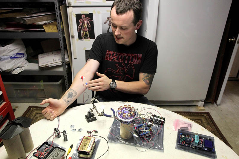 Thomas Lemieux flexes his forearm, attached with an electrode, to activate a bionic repulsor, while working on his life-size Iron Man costume in the basement of his Oakland home recently.